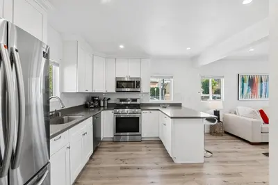 a kitchen with white cabinets and a stainless steel refrigerator at Muirfield Chic City Bungalow with Parking 1,2,3 in Los Angeles