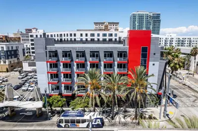 a red building in a city with palm trees and a bus at Hotel Mai Downtown Long Beach in Long Beach