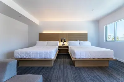 a bedroom with two beds and a chair and a window at Hotel Mai Downtown Long Beach in Long Beach