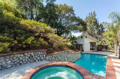 a swimming pool with a stone wall next to a house at NEW Modern apt w/pool & hot tub in nature in Thousand Oaks