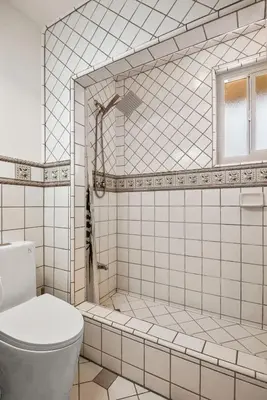 a white tiled bathroom with a toilet and a shower at Luxury 6BR Retreat Fast WIFI, Dedicated Workspaces in Hesperia