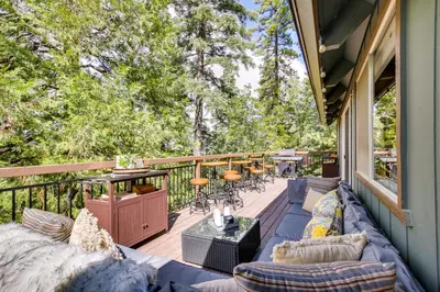 a porch with blue couches and tables and trees at Cozy and Chic Lake Arrowhead Cabin with Deck! in Lake Arrowhead
