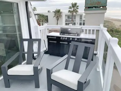 a grill on a porch with two chairs and a stove at Oceanfront Penthouse On Sand - Epic Views/Sunsets! in Huntington Beach
