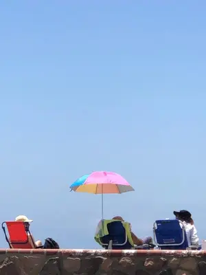 a group of people sitting on the beach with an umbrella at The Shores Inn in Ventura