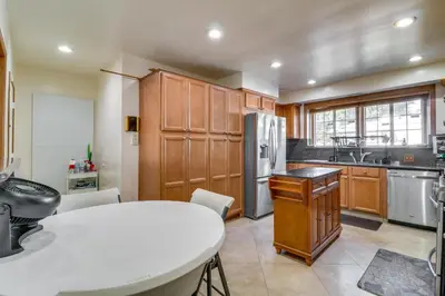 a kitchen with wooden cabinets and a white table at North Hills Home with Outdoor Entertaining Space in North Hills