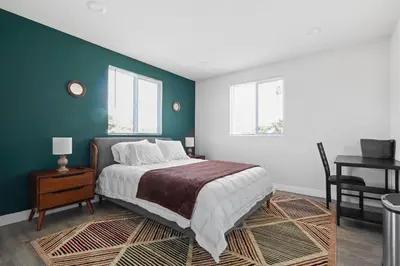 a bedroom with a bed and a desk and two windows at Good Shepard Homestay in Los Angeles