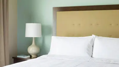 a bed with white pillows and a lamp on a table at Homewood Suites by Hilton San Bernardino in San Bernardino