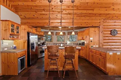 a kitchen with wooden cabinets and bar stools at Peaceful Cabin Home with Breathtaking View! in Big Bear City
