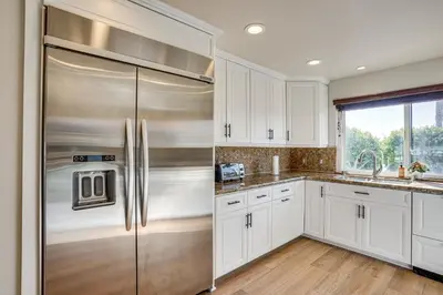 a kitchen with white cabinets and a stainless steel refrigerator at Huntington Beach Condo - Walk to the Ocean! in Huntington Beach