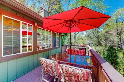 a table and chairs on a porch with a red umbrella at Creekside Cabin in Crestline