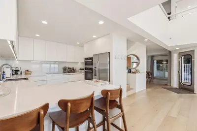 a kitchen with white cabinets and a island with chairs at Malibu Breeze - hot tub, ocean view, steps to beach in Malibu