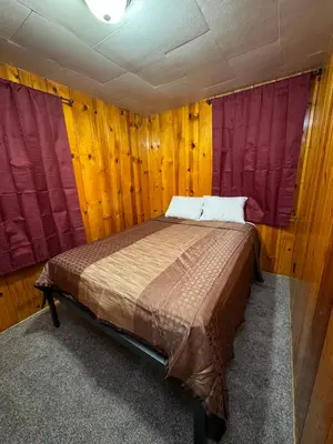 a bed in a room with wooden walls and windows at Crest Lodge Historic Mountain Inn in Crestline