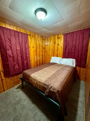 a bed in a room with wooden walls and red curtains at Crest Lodge Historic Mountain Inn in Crestline