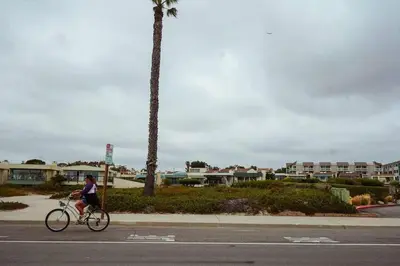 a person riding a bike down a street with a palm tree at SeaView, Pool, HotTub, W/D, Bikes, Gated Community in Port Hueneme