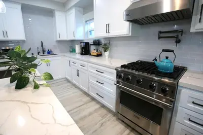 a kitchen with white cabinets and a stove with a tea kettle on it at Steps 2 Beach- Luxury Home, Game Room, Roof Deck, Firepit, Pets OK in Oxnard