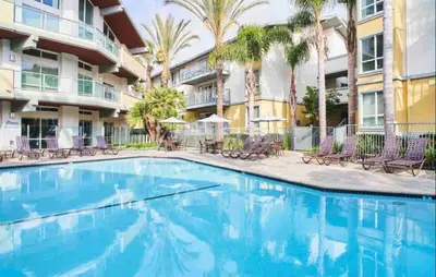 a swimming pool in front of a building with palm trees at Sunny Condo with Panoramic Ocean Views in Los Angeles