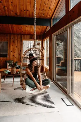 a woman sitting in a rattan chair in a living room at Lightfoot Cabin Mid-Century Perfect Romantic Getaway Hot Tub Sauna in Running Springs