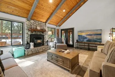 a living room with a fireplace and a stone wall at Evergreen -LUXURY CABIN WITH A HOT TUB, GAME ROOM & 3 EN-SUITE BEDROOMS! in Big Bear Lake