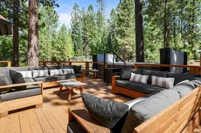 a deck with couches and a television and trees at Evergreen -LUXURY CABIN WITH A HOT TUB, GAME ROOM & 3 EN-SUITE BEDROOMS! in Big Bear Lake