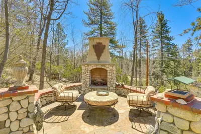 a patio with a stone fireplace in the woods at Lake Arrowhead Home Mountain View, Walk to Water! in Lake Arrowhead