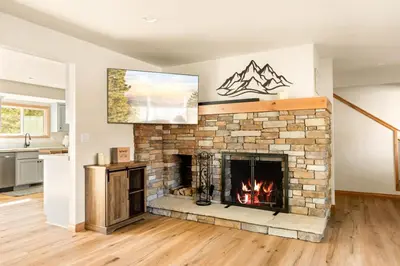 a living room with a brick fireplace with a painting at Lakeside Paradise Escape in Big Bear Lake