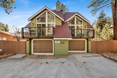 a green house with a balcony and two garage doors at Fawnskin Chalet#1826 in Fawnskin