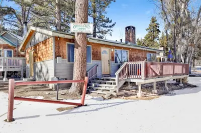 a house in the snow with a sign on a tree at Shore acres lodge #450 in Big Bear Lake