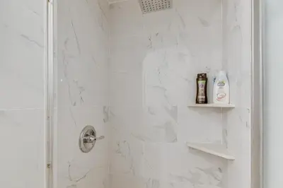 a bathroom with a shower with white marble tiles at 1 Mi to Melrose Ave and Grove! Upscale LA Retreat in Los Angeles