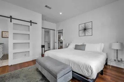 a white bedroom with a large bed and a stool at Gramercy Getaway in Los Angeles