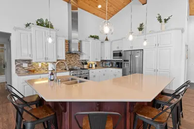 a kitchen with white cabinets and a large island with bar stools at Modern Lakefront Dream Home Steps from Big Bear Village in Big Bear Lake