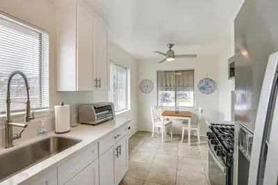 a kitchen with white cabinets and a sink and a table at 2 Mi to Ocean! Executive-Style Oasis in Long Beach in Long Beach