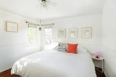 a white bedroom with a white bed with red pillows at Silver Lake Mid-century Nestled in the Treetops in Los Angeles