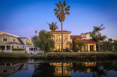 a house with a palm tree in front of a body of water at The Canal Escape - canal-front Italian villa in Los Angeles