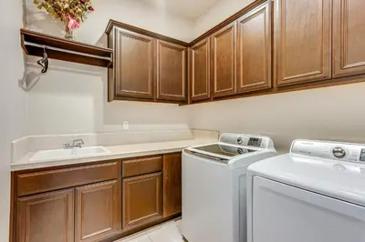 a kitchen with wooden cabinets and a washer and dryer at Beautiful Bakersfield Home about 8 Mi to Downtown! in Bakersfield