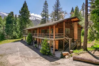 a log cabin in the woods with mountains in the background at Camp Nelson Lodge Room 9 in Ponderosa