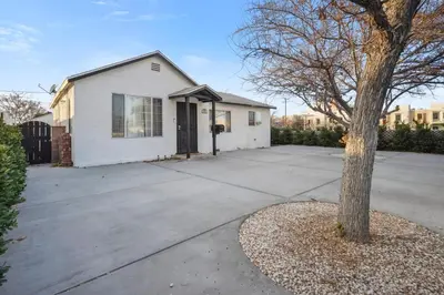 a white house with a tree next to a driveway at Cozy single story 2 bdrm family home near the BLVD in Lancaster