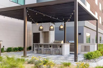 an outdoor kitchen with pendant lights and a pergola at Homewood Suites by Hilton Cypress Orange County in Cypress