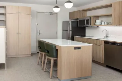 a kitchen with wooden cabinets and a kitchen island with green chairs at Homewood Suites by Hilton Cypress Orange County in Cypress