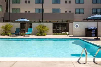 a swimming pool with chairs and umbrellas next to a building at Homewood Suites by Hilton Cypress Orange County in Cypress