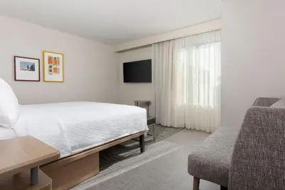 a bedroom with a bed and a chair and a television at Homewood Suites by Hilton Cypress Orange County in Cypress