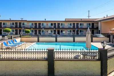 a swimming pool with chairs and an umbrella and a building at Sea Rock Inn - Los Angeles in Los Angeles
