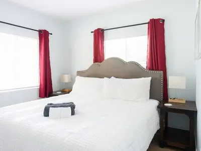 a white bed with red curtains and a bag on it at Family Renovated Home, Netflix, AC, WD, Putt Putt in Fullerton