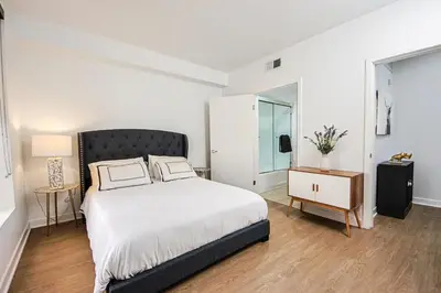 a white bedroom with a bed and a night stand at The Carlton - Modern-Lux 2 Master Suites-Secure Bldg & Parking- 5 BLKS to Ocean Ave in Los Angeles