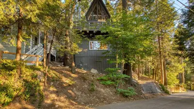a house in the woods with a tree at A-Frame Retreat Chic and Modern Forest Views Hammock Outdoor Dining Decks in Lake Arrowhead