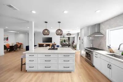 a kitchen with white cabinets and a living room at NEW Lux 5BR Villa Near Disney, Knotts, LA, OC with Hot Tub & Games in Fullerton