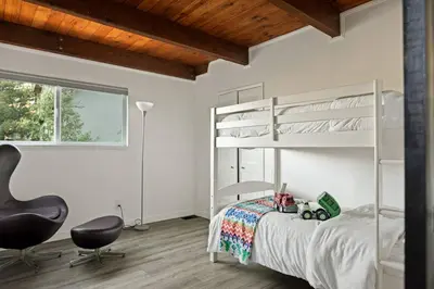 a bedroom with a white bunk bed and a chair at Quiet Mountain Cabin in Lake Arrowhead