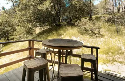 a wooden table and two stools on a deck with a table at Sprocket Hollow Treetop A-Frame Log Cabin in Cedar Glen
