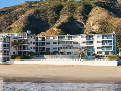 a building on the beach with a mountain in the background at Aquamarine Best View in Malibu by Stay Awhile Villas in Malibu Beach