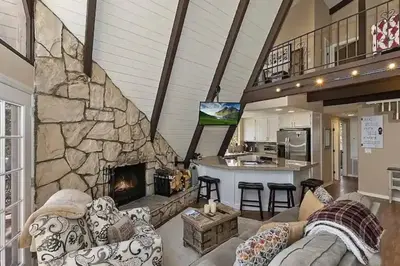 a living room with a large stone fireplace at Whispering Pines A-Frame, Pool Table, 2 Patios! in Lake Arrowhead