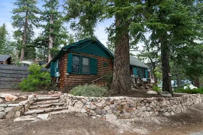 a log cabin with a tree and a stone wall at Mountain Cottage - Hot Tub! Walk to Lake and National Forest Hiking Trails in Big Bear Lake